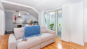 Eine moderne Wohnung mit Küchenzeile, einem Sofa mit blauer Decke und Blick durch eine Glastür nach draußen.