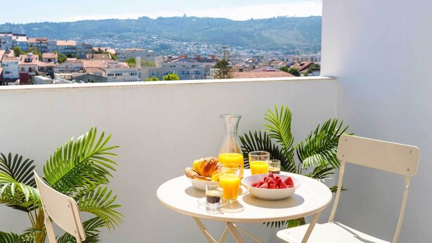 Ein Balkon mit Frühstückstisch, komplett mit Croissants, Obst und Saft, mit Blick auf eine Stadtlandschaft.