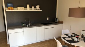 Una cocina moderna con armarios blancos, encimera negra y comedor con mesa y sillas blancas.