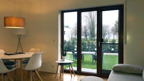 Una habitación moderna con una mesa de comedor, sillas, un sofá y un amplio ventanal corredera que da a un área exterior.