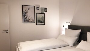 Un dormitorio con cama, mesita de noche, lámpara de pared y cuadros enmarcados.