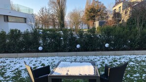 Un patio con una mesa y dos sillas, rodeado de nieve en el suelo.