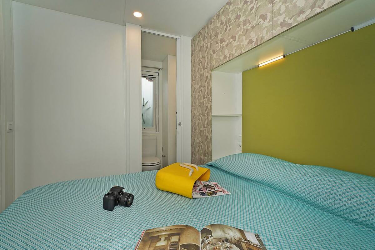 A bedroom with a checkered bedspread, a camera, and a yellow bag on the bed.