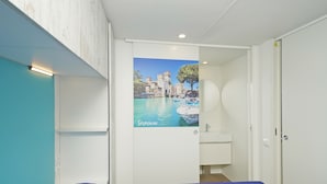 Een slaapkamer met een bed, een poster van een kasteel, een badkamer met een wastafel en een witte kledingkast.