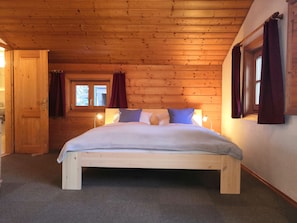 A wooden-paneled bedroom with a bed, two windows, and a door.