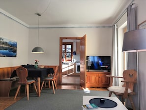 A cozy living room with a dining area, wooden furniture, a TV, and a view into the kitchen.