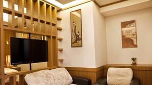 A modern hotel room with a sofa, a chair, a flat-screen TV, wooden paneling, and artwork on the walls. - Jia Xin Hot Spring Resort Yangming Shan (New Taipei City)