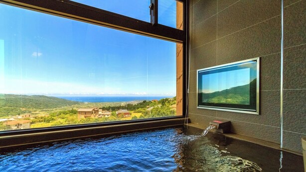 A room with a large window overlooking a scenic landscape, a bathtub filled with water, and a framed picture on the wall. - Jia Xin Hot Spring Resort Yangming Shan (New Taipei City)