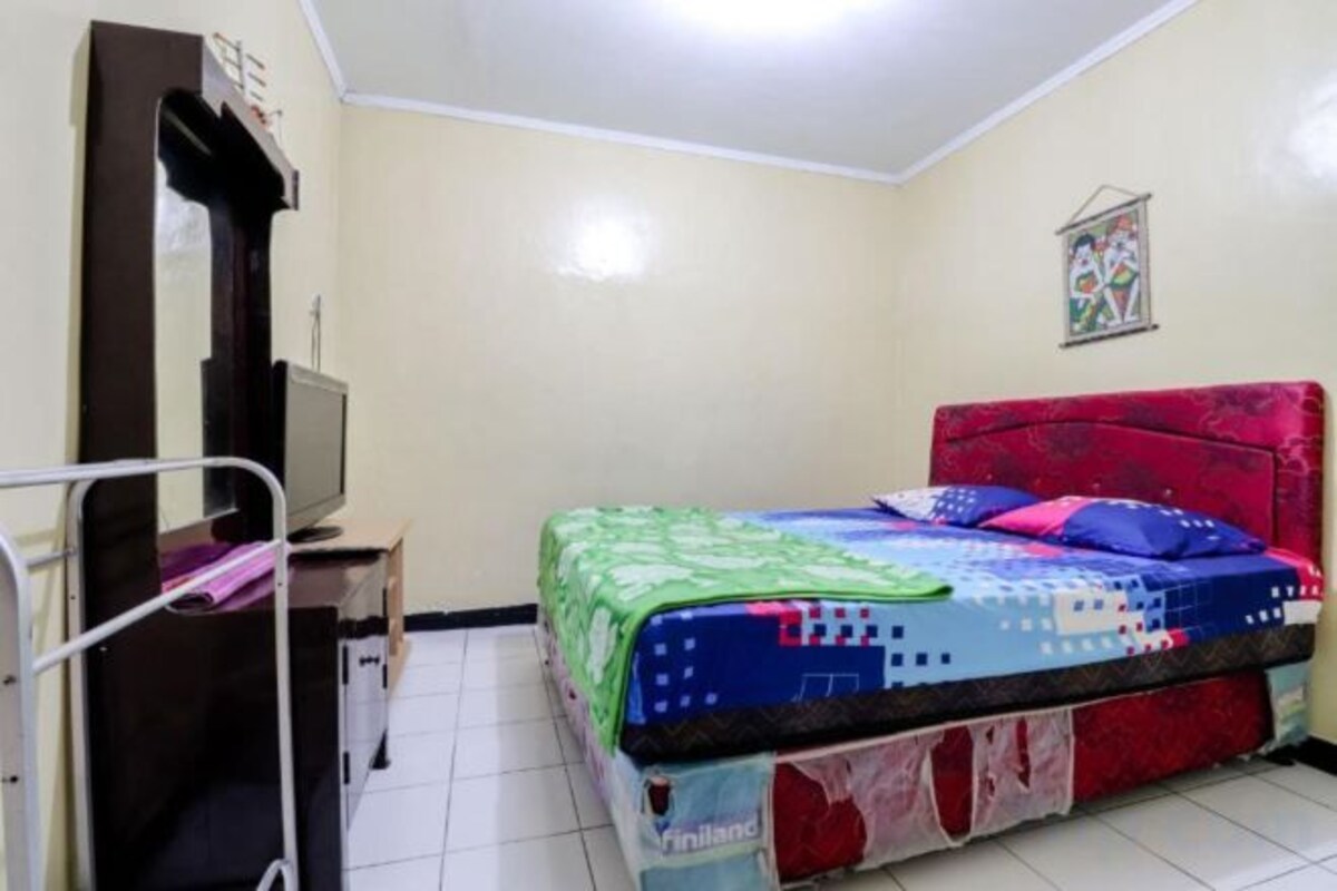 A room with a bed, a desk with a computer, a mirror, and a wall decoration.