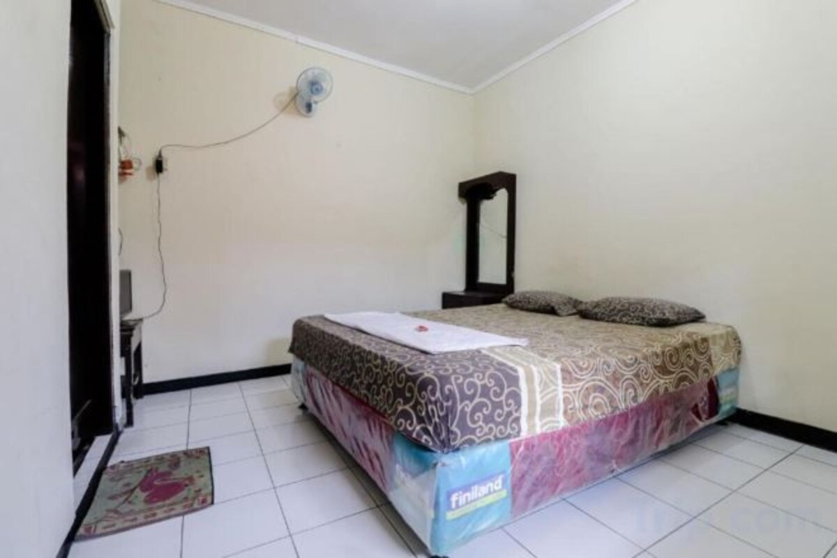 A bedroom with a bed, a bedside table, a mirror, and a wall-mounted fan.