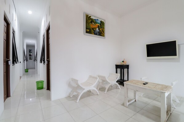 A hallway with white walls, a painting, a TV, and a table with chairs.