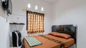 Ein ordentlich eingerichtetes Schlafzimmer mit einem Bett, einem Heizkörper, einem Fenster mit Vorhängen und einem an der Wand befestigten Fernseher.