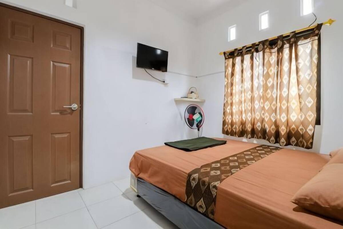 A bedroom with a bed, a television, a fan, and a door.