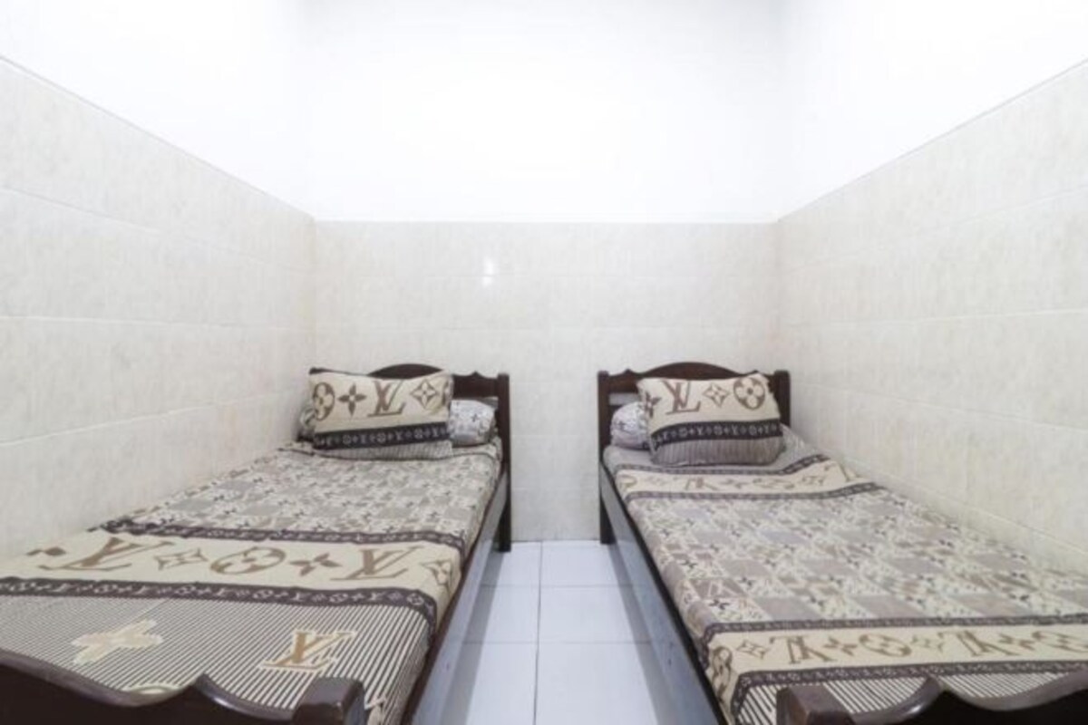 Una habitación pequeña y estrecha con dos camas individuales, cada una con ropa de cama y almohadas estampadas.
