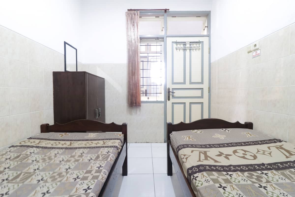 A small, clean room with two beds, a wardrobe, and a door leading to another room.