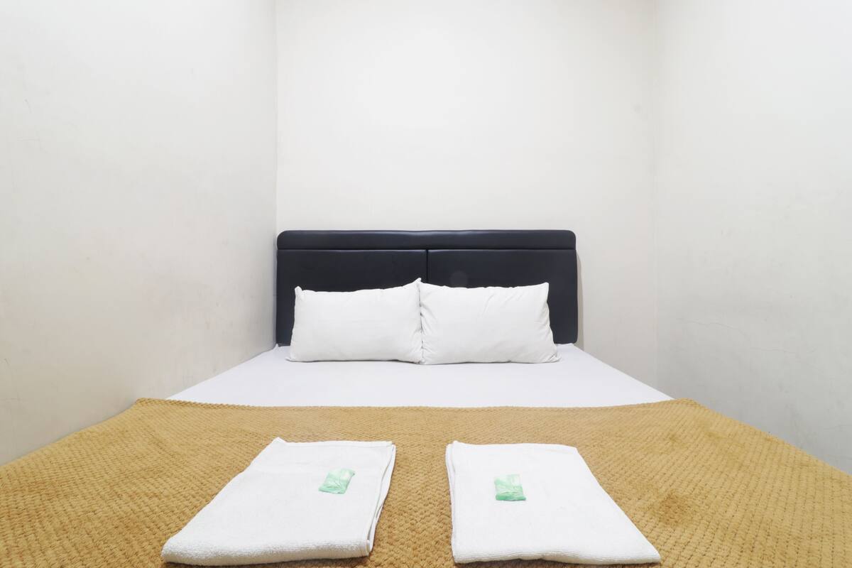 A single bed with a dark headboard, white bedding, and two folded towels on a textured brown rug.