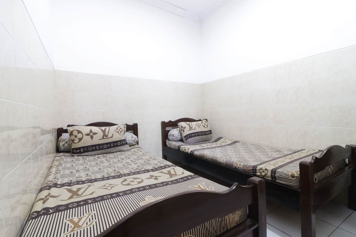 A small, clean room with two single beds, each with patterned bedding and wooden headboards.