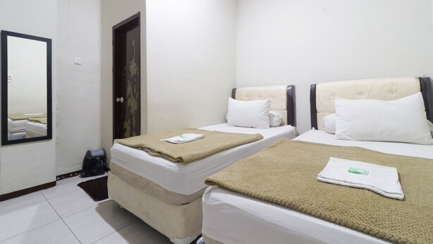 A hotel room with two beds, each with a beige blanket and white pillows. There is a mirror on the wall and a door to the left.