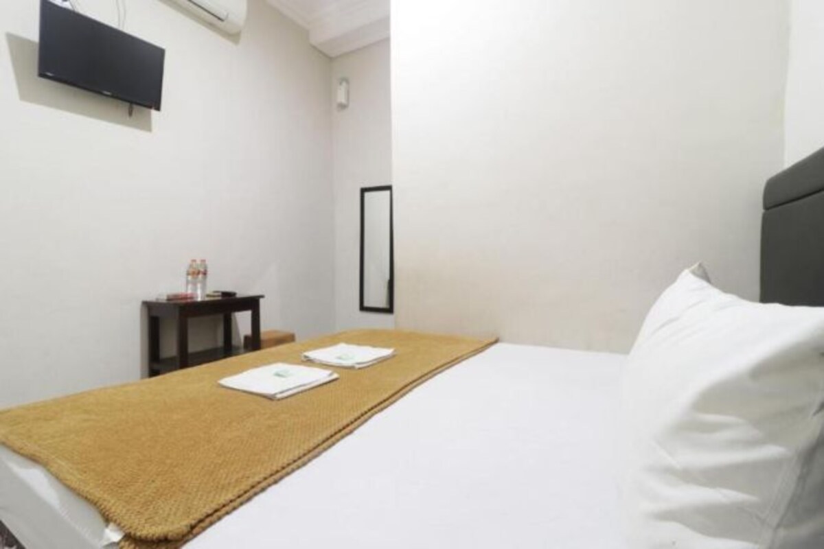 Habitación de hotel con cama, una mesita con una botella y vasos, un televisor montado en la pared y un cuadro enmarcado.