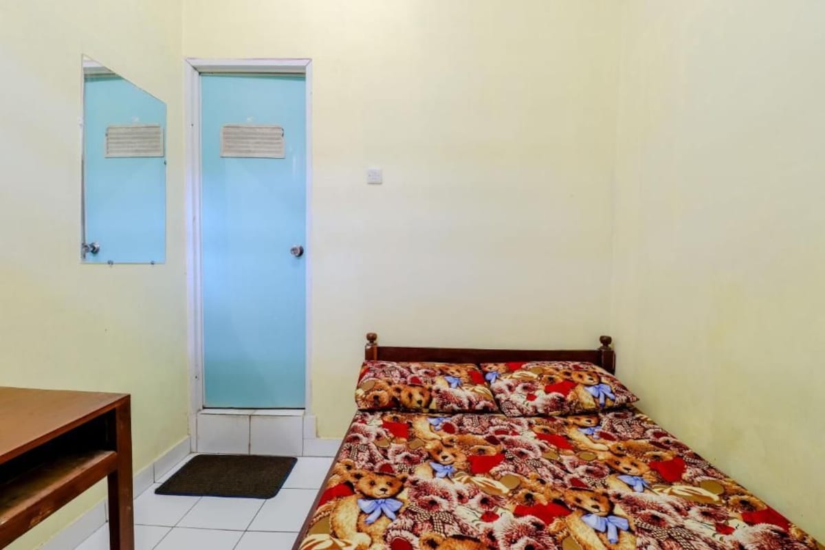 Ein Zimmer mit einem Bett, einem Holztisch, einer blauen Tür und einem kleinen Teppich.