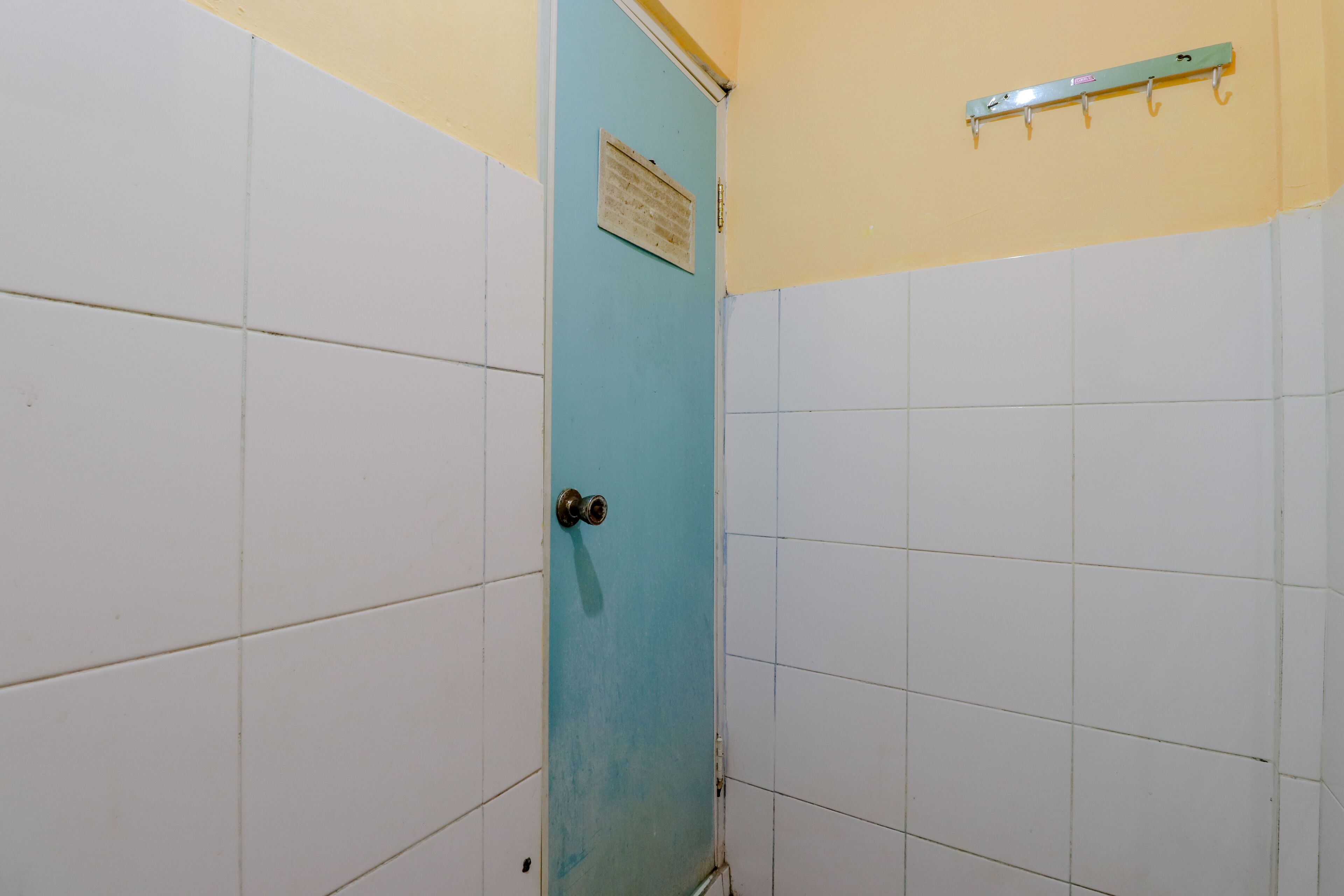 Un bagno con pareti piastrellate di bianco, una porta blu e un porta asciugamani in metallo a parete.