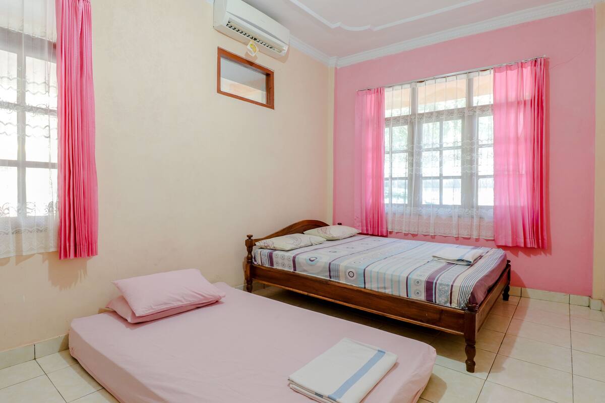 Een slaapkamer met een enkel bed, een raam met roze gordijnen en een airconditioner aan de muur.