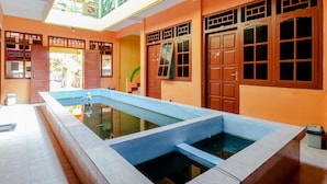 Una piscina con borde de baldosas, puertas de madera y un balcón con barandilla verde.