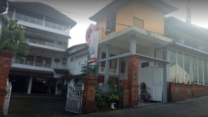 A multi-story building with a gated entrance, a covered area with potted plants, and a visible sign. - Wisma & Kantin Amanda (Pacet)