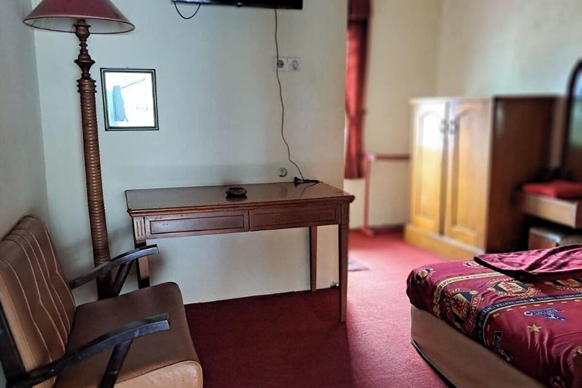 A hotel room with a bed, a desk, a chair, a TV mounted on the wall, and a wardrobe.