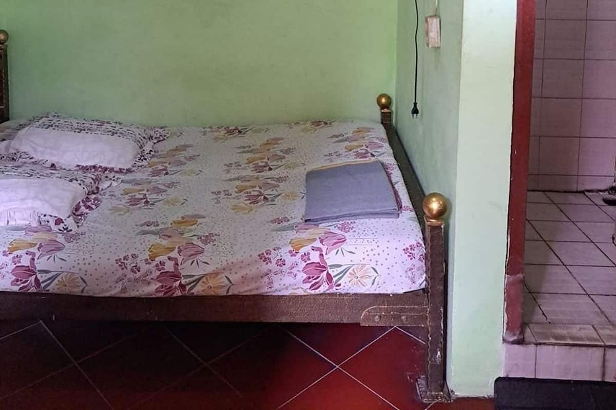A single bed with a floral bedspread in a room with green walls and a tiled floor.