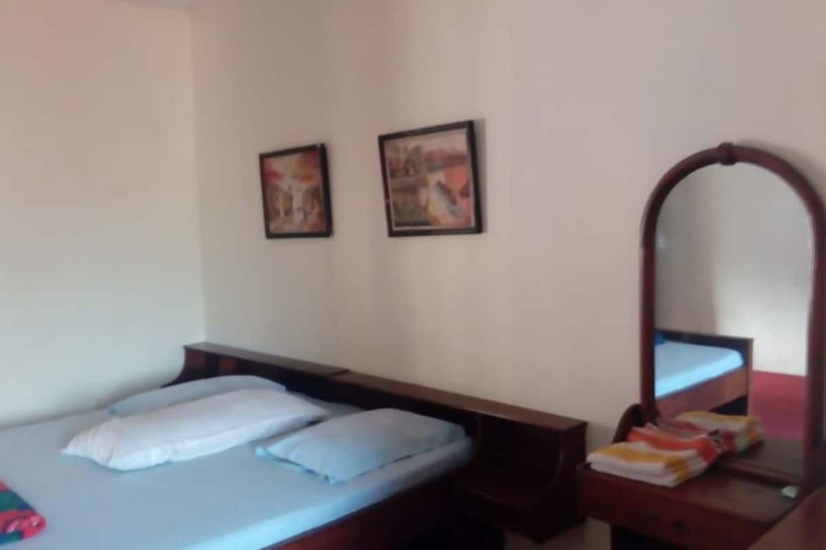 A bedroom with a bed, a nightstand, a mirror, and two framed pictures on the wall.