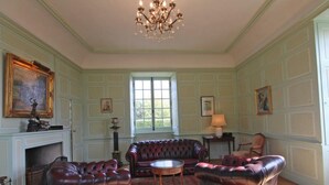 A spacious room with a fireplace, leather sofas, a chandelier, and a large window. - Chaplain's House: Charm in Swiss Normandy, Pets Allowed (Rabodanges)