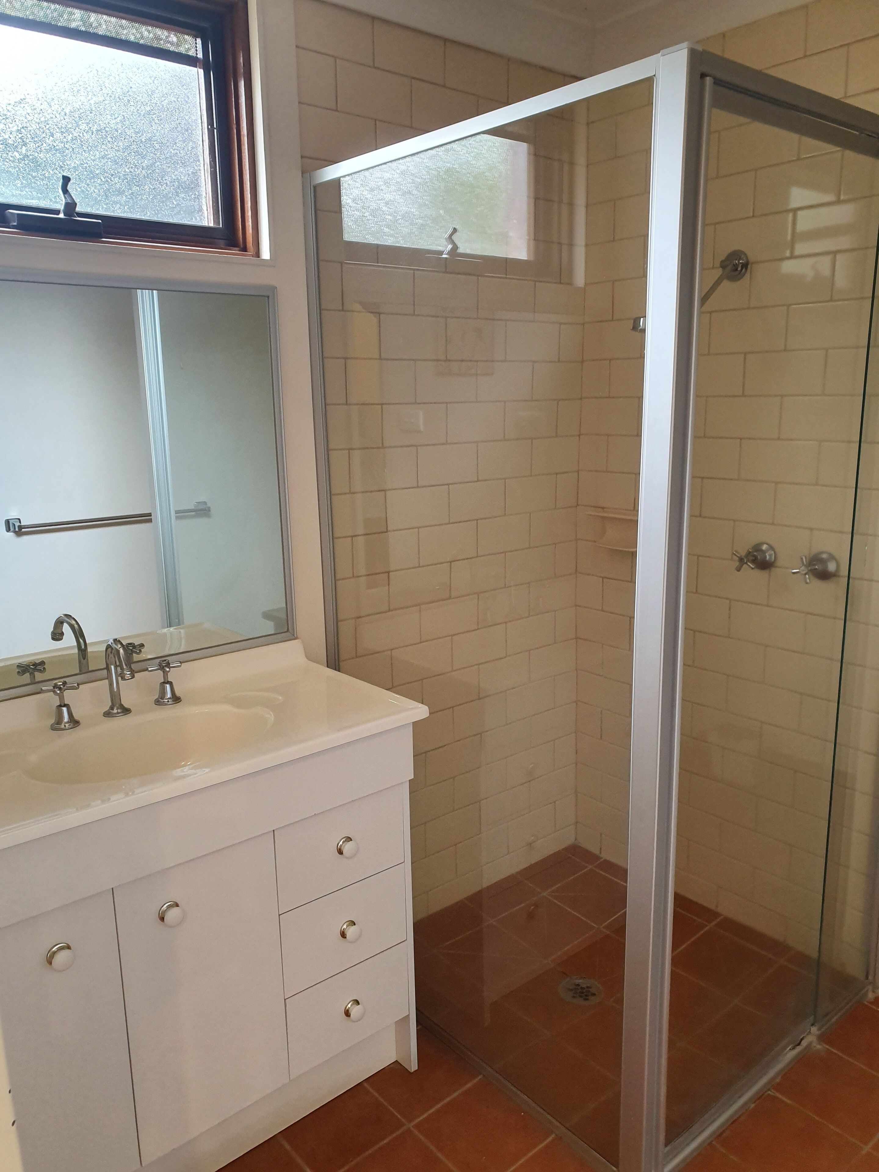 A bathroom with a glass-enclosed shower, a white sink with two faucets, and a mirror above the sink.