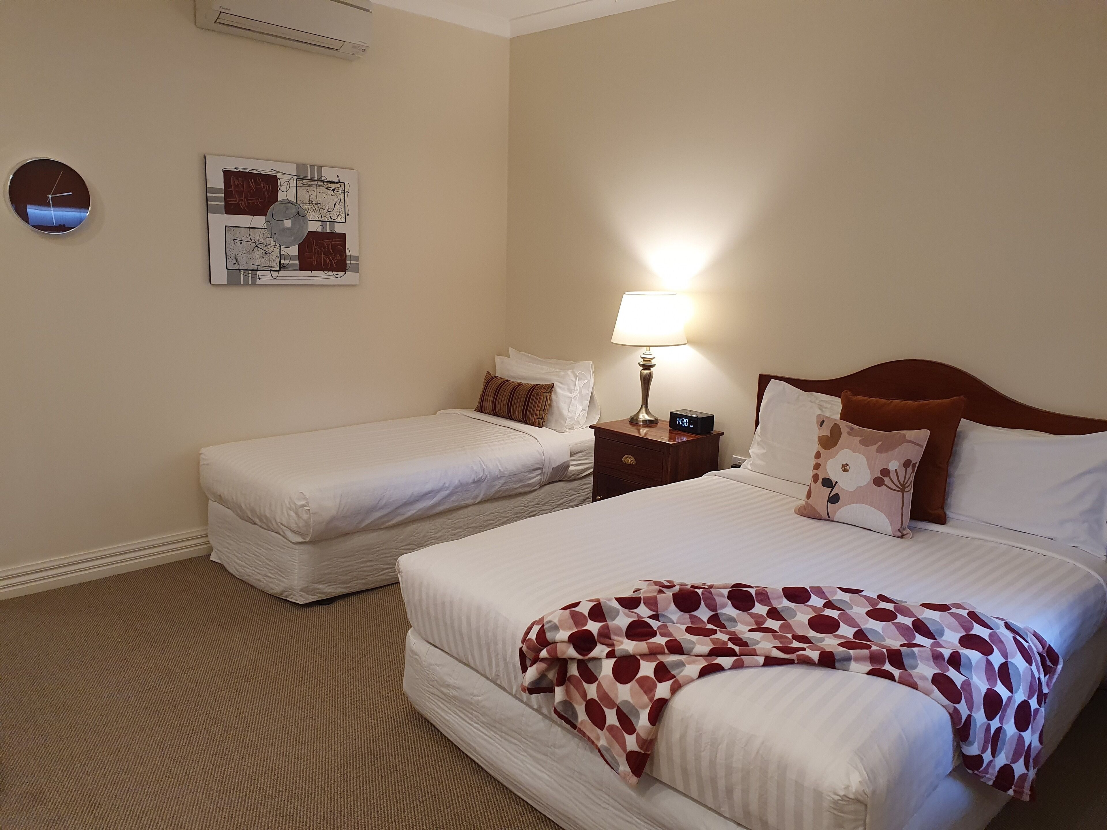 Habitació d'hotel amb dos llits, una tauleta de nit amb una làmpada, un rellotge i obra d'art a la paret.