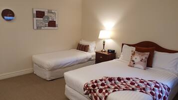 Habitació d'hotel amb dos llits, una tauleta de nit amb una làmpada, un rellotge i obra d'art a la paret.