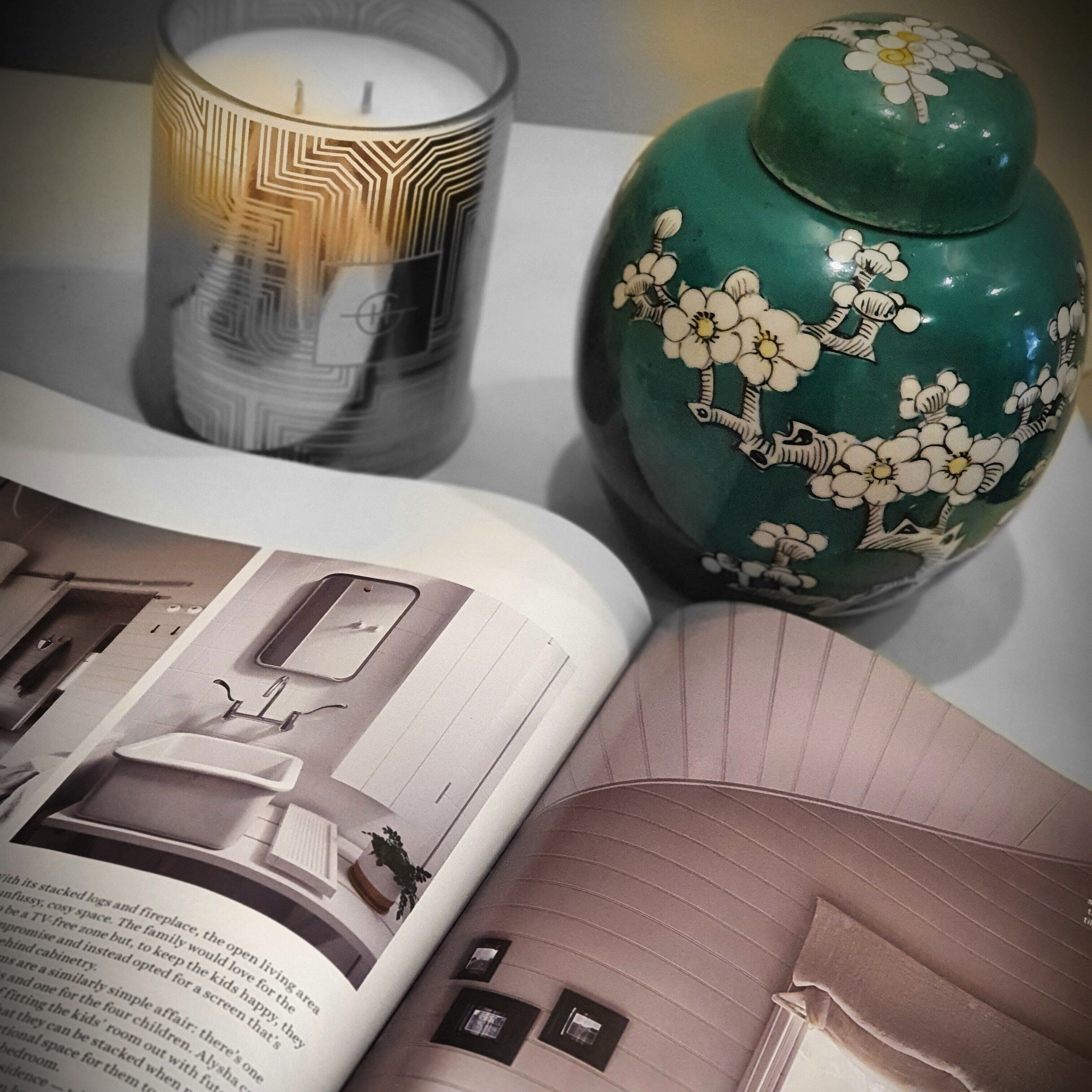 Un libro abierto mostrando un plano de una habitación, una vela y un jarrón decorativo.