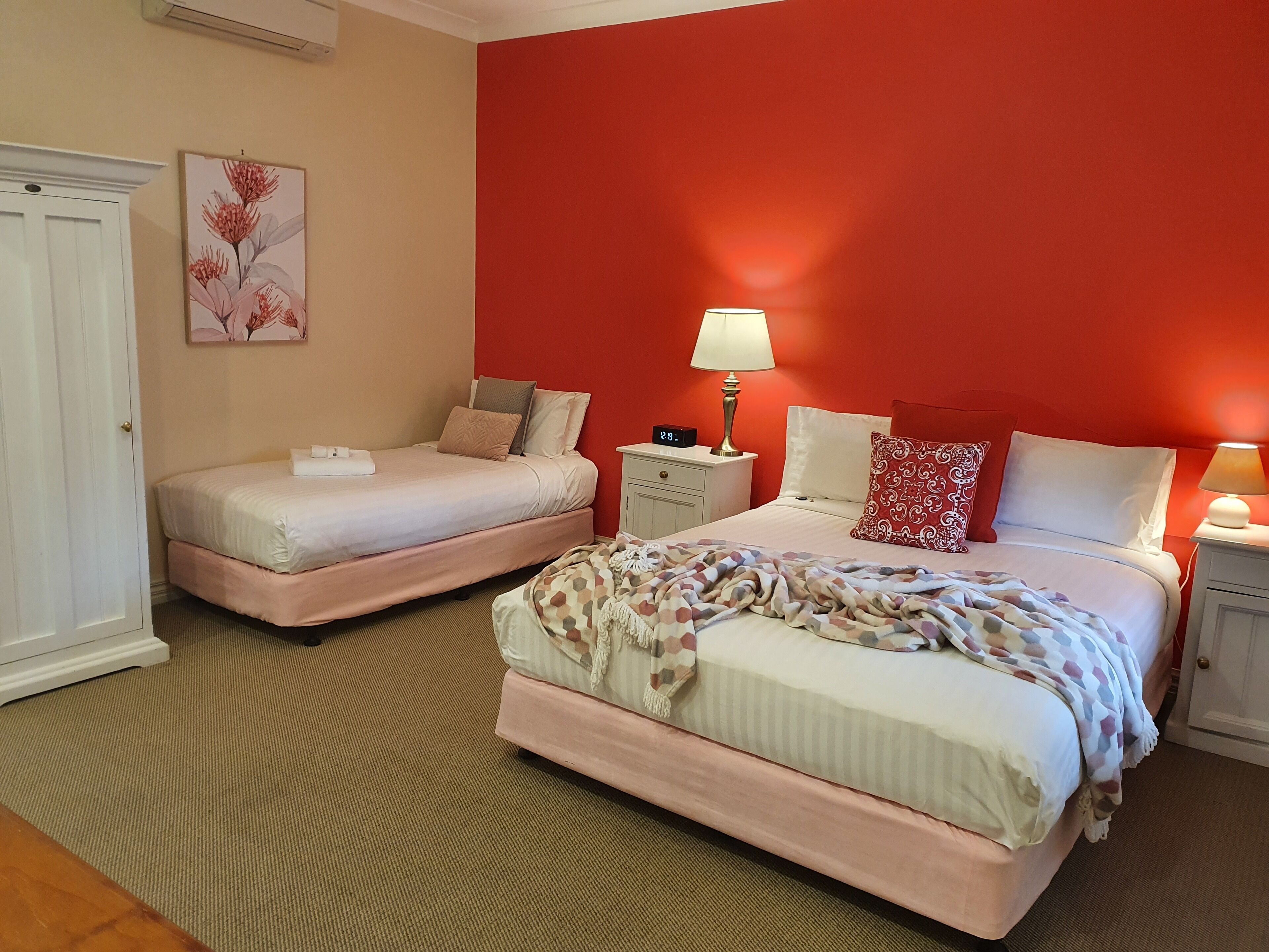 A hotel room with two beds, a nightstand with a lamp, a wall clock, and a framed botanical print.