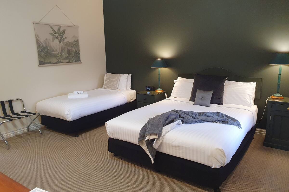 A hotel room with two beds, each with white linens and pillows, a dark headboard, bedside lamps, a small table, and a chair.