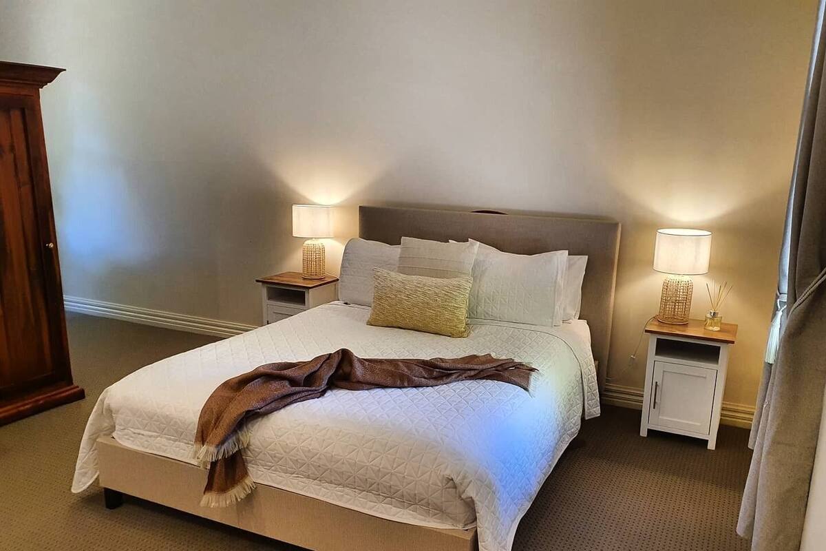 A neatly made bed with a brown throw blanket, two bedside lamps, and a wooden nightstand.