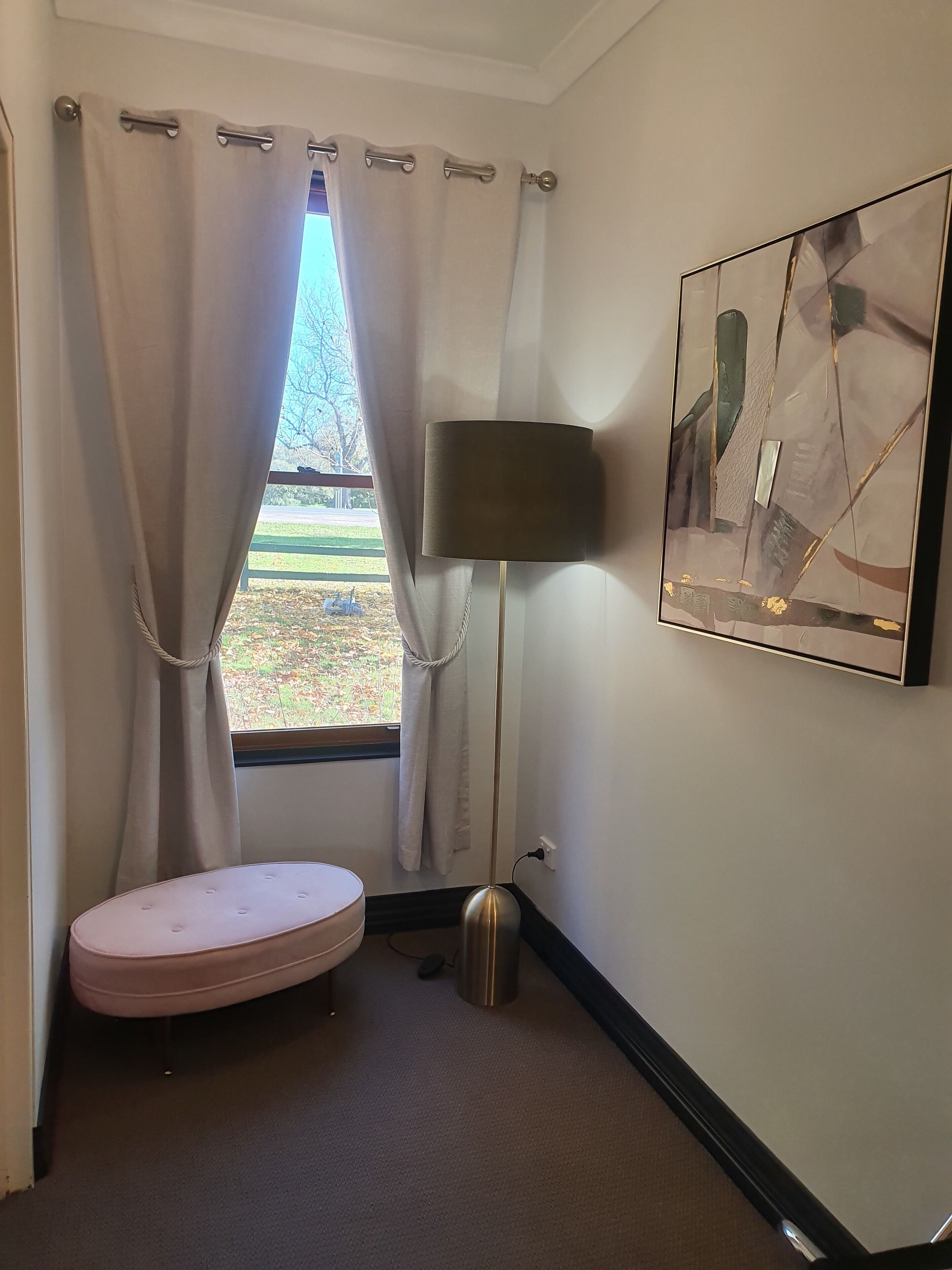 Una habitación con ventana, un banco rosa, una lámpara de pie y una obra de arte abstracta en la pared.