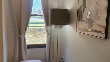 Una habitación con ventana, un banco rosa, una lámpara de pie y una obra de arte abstracta en la pared.