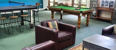 A room with a pool table, leather sofas, and a billiards table.