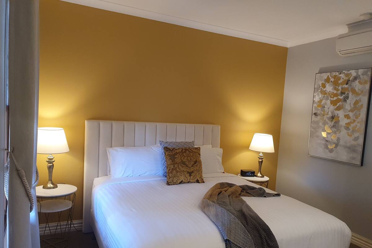 A hotel room with a large bed, two bedside lamps, a clock, and a wall-mounted artwork.