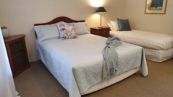 A hotel room with a large bed, a smaller bed, a nightstand with a lamp, a wooden side table, and a framed picture on the wall.