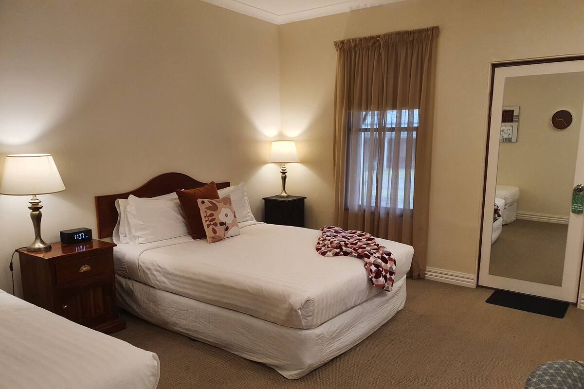 A hotel room with a bed, bedside lamps, a clock, a mirror, and a door.