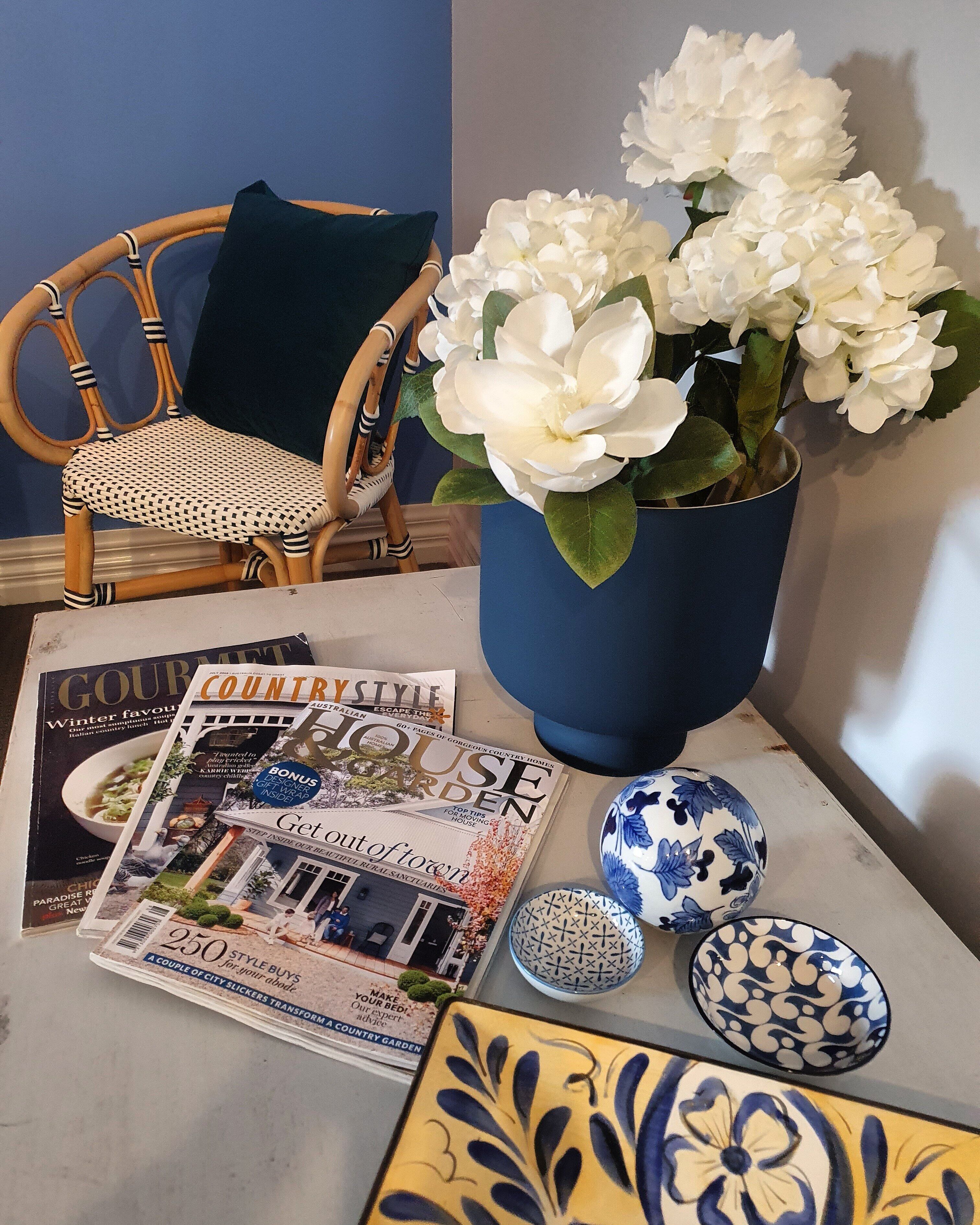 A magazine spread with a wicker chair, a vase of white flowers, and decorative bowls.