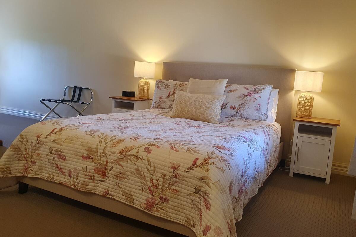 A neatly made bed with floral bedding, two bedside lamps, and a small white nightstand with a radio.