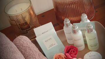 Ett bricka med toalettartiklar, inklusive ett lavendeldoftande ljus, en glasvas med rosa blommor och olika produkter från Bath & Body Works.