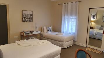 A hotel room with two beds, a desk with a chair, a window with curtains, and a mirror on the wall.