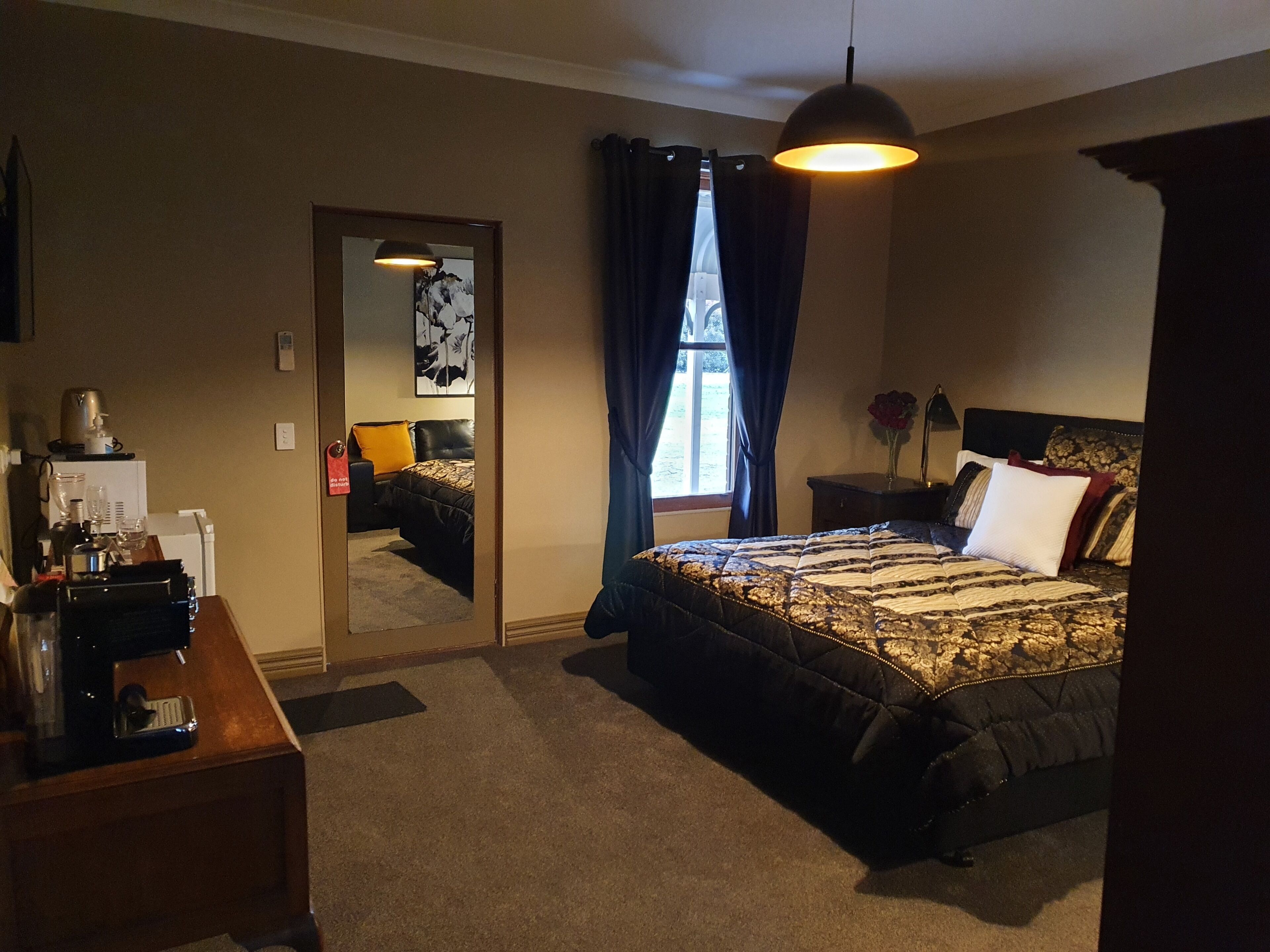 Un dormitorio con cama, escritorio, espejo, ventana con cortinas e iluminación colgante.